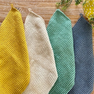 K&ouml;nnte beinhalten: F&uuml;nf geh&auml;kelte Geschirrt&uuml;cher in verschiedenen Farben: Gelb, Wei&szlig;, Gr&uuml;n und Blau. Die Geschirrt&uuml;cher h&auml;ngen an einer Holzoberfl&auml;che.