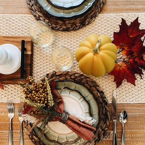 May include: A fall-themed table setting with a woven placemat, a green and white patterned plate, a red napkin, a small bouquet of berries, and a yellow pumpkin.