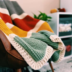 May include: A multi-colored striped crocheted throw blanket with a cream colored border draped over a brown leather chair.