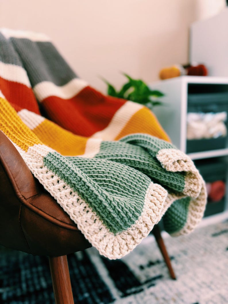 May include: A multi-colored striped crocheted throw blanket with a cream colored border draped over a brown leather chair.