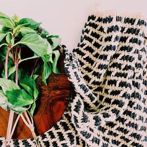 May include: A bunch of green basil leaves on a wooden cutting board with a black and white crocheted dishcloth in the background.