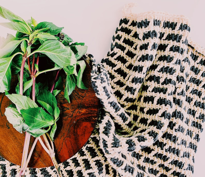 May include: A bunch of green basil leaves on a wooden cutting board with a black and white crocheted dishcloth in the background.