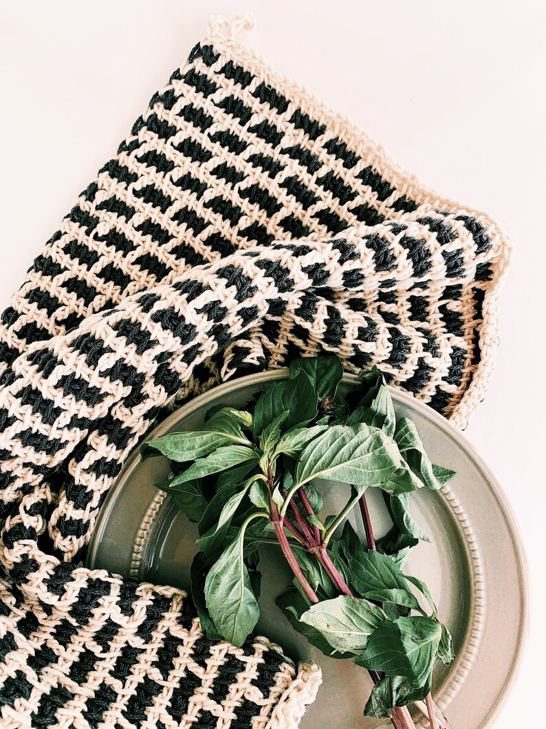 May include: A bunch of fresh green basil leaves on a gray ceramic plate with a black and cream striped crocheted dishcloth.