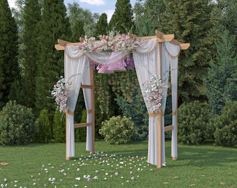May include: A white wedding archway decorated with pink and white flowers and sheer white fabric drapes. The archway is set up outdoors in a grassy area with green trees in the background.