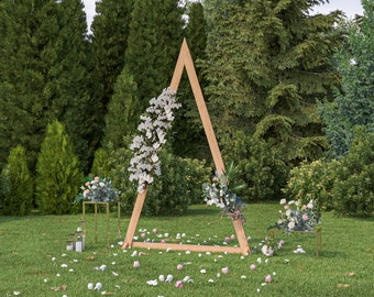 May include: A wooden triangular archway decorated with white and pink flowers, set up outdoors on a grassy lawn with green trees in the background.