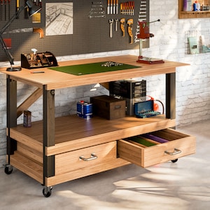 May include: A wooden workbench with a green work surface, two drawers, and a lower shelf. The workbench is on wheels and has black metal legs and supports. The workbench is in a workshop setting with a brick wall in the background.