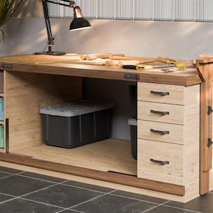 Puede incluir: Un gran banco de trabajo de madera con cajones y compartimentos de almacenamiento. El banco de trabajo tiene una parte superior de madera oscura y laterales de madera clara. Las herramientas y una lámpara están en la superficie. Hay tres contenedores de almacenamiento de colores y un gran contenedor de almacenamiento gris.