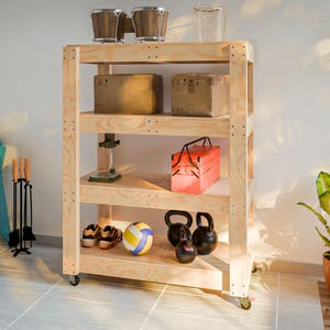 Pode incluir: Uma unidade de armazenamento rolante de madeira de quatro prateleiras com uma variedade de itens nas prateleiras, incluindo caixas, ferramentas, uma caixa de ferramentas vermelha, uma bola de voleibol e duas kettlebells.