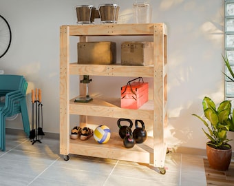 Puede incluir: Una unidad de almacenamiento rodante de madera de cuatro estantes con una variedad de artículos en los estantes, que incluyen cajas, herramientas, una caja de herramientas roja, un balón de voleibol y dos pesas rusas.