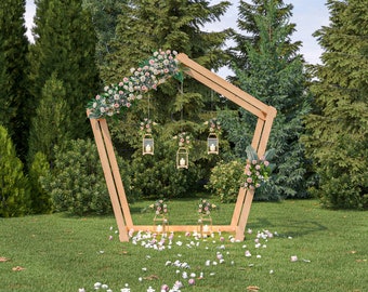 May include: A wooden wedding arch decorated with pink flowers and hanging lanterns. The arch is set up in a grassy area with trees in the background.