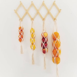 May include: Five hanging fruit bags with a variety of fruits, including oranges, lemons, and apples. The bags are made of natural twine and are hanging from a wooden wall rack.