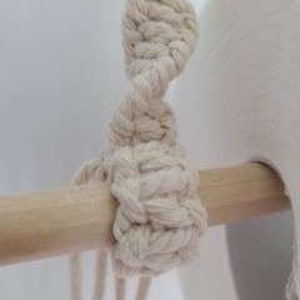 Puede incluir: Primer plano de un nudo macram&eacute; atado alrededor de una varilla de madera. El nudo est&aacute; hecho con cord&oacute;n de algod&oacute;n de color natural.