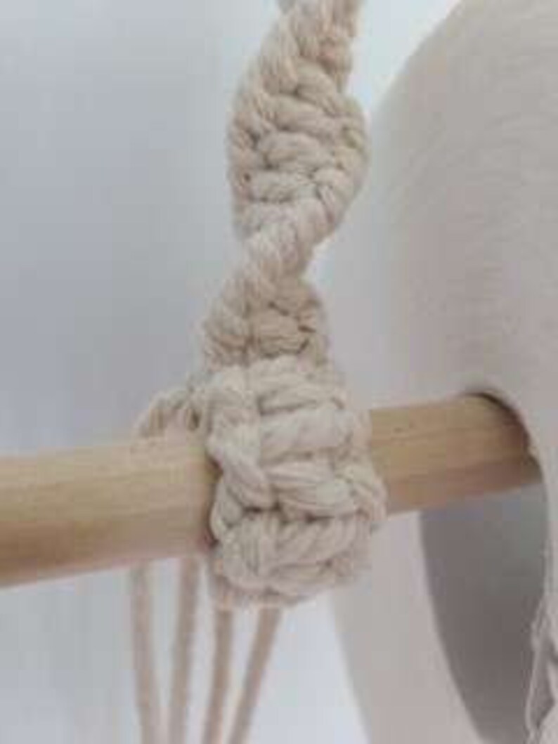 Puede incluir: Primer plano de un nudo macram&eacute; atado alrededor de una varilla de madera. El nudo est&aacute; hecho con cord&oacute;n de algod&oacute;n de color natural.