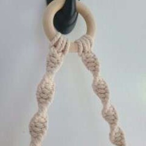 Puede incluir: Primer plano de un macram&eacute; para colgar plantas con un anillo de madera. El macram&eacute; est&aacute; hecho de cuerda de algod&oacute;n natural y tiene un dise&ntilde;o en espiral. El macram&eacute; est&aacute; sujeto a un gancho negro.
