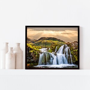 May include: A framed photograph of a waterfall cascading down a mossy hillside. The sun shines through the clouds, creating a dramatic light effect. The image is in a black frame.