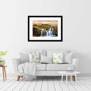 May include: A framed photograph of a waterfall cascading over moss-covered rocks in a lush green landscape. The sky is a soft blue with white clouds.