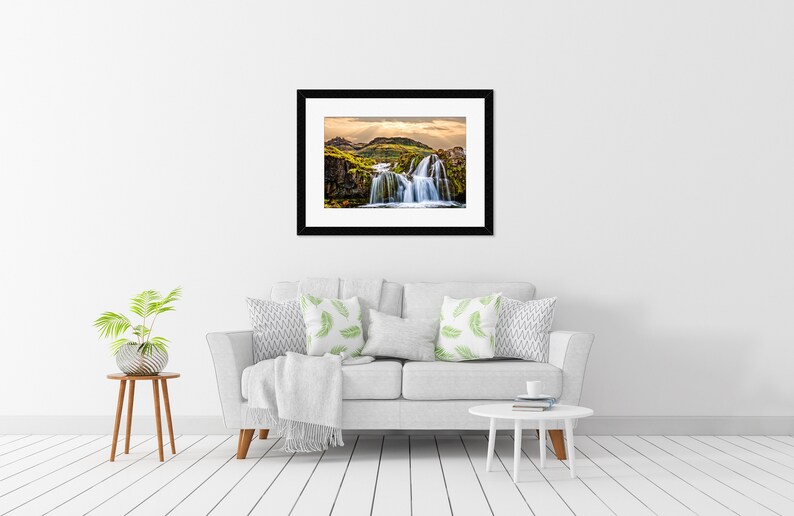 May include: A framed photograph of a waterfall cascading over moss-covered rocks in a lush green landscape. The sky is a soft blue with white clouds.