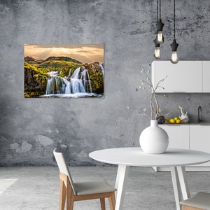 May include: A photograph of a waterfall cascading down a rocky cliff face. The waterfall is surrounded by lush green vegetation and the sky is a bright blue with white clouds. The image is taken from a low angle, giving the viewer a sense of the waterfall's power and beauty.