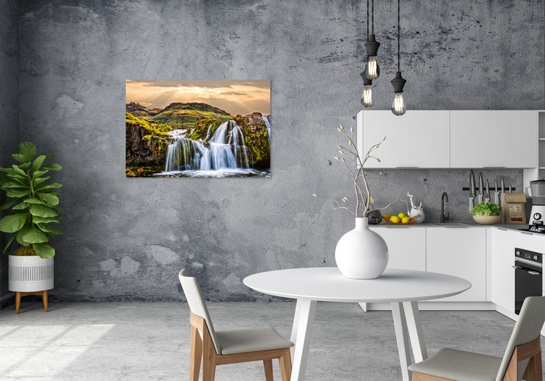 May include: A photograph of a waterfall cascading down a rocky cliff face. The waterfall is surrounded by lush green vegetation and the sky is a bright blue with white clouds. The image is taken from a low angle, giving the viewer a sense of the waterfall's power and beauty.