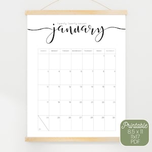 Puede incluir: Un calendario de pared para enero de 2027 con un diseño de cuadrícula minimalista en blanco y negro y el nombre del mes en elegante letra cursiva. El calendario se sujeta con listones magnéticos de madera clara y tiene un cordel.