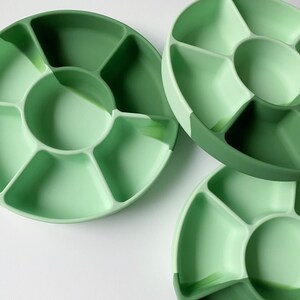 May include: Three green divided serving dishes with a circular center section and six smaller sections around the center. The dishes are made of silicone and are perfect for serving snacks, dips, or condiments.