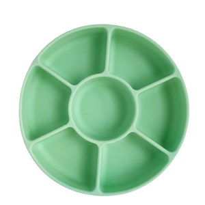 May include: A light green silicone divided dish with six sections. The dish is round and has a raised center section.