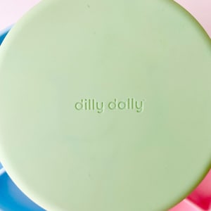May include: A light green silicone lid with the text "dilly dally" embossed on the top.