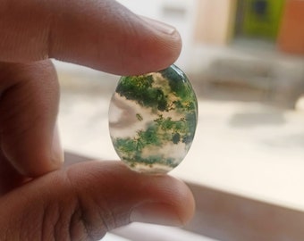 May include: A green and white agate cabochon with a mossy pattern. The stone is oval shaped and has a smooth, polished surface.