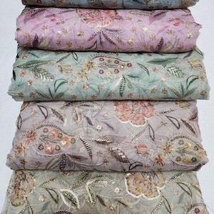 May include: A stack of fabric rolls in various pastel colors, including light blue, lavender, and sage green. Each roll is adorned with intricate floral embroidery, sequins, and metallic thread, creating a luxurious and textured appearance. The fabric is likely suitable for apparel or decorative projects.