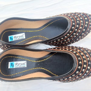 May include: Pair of black flat shoes with silver and orange embellishments. The shoes have a label that reads "Royal Collection".