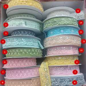 May include: A collection of spools of decorative ribbon in various colors, including yellow, green, pink, and blue. The ribbons feature intricate designs with pearls and reflective accents, suitable for crafts and embellishments.
