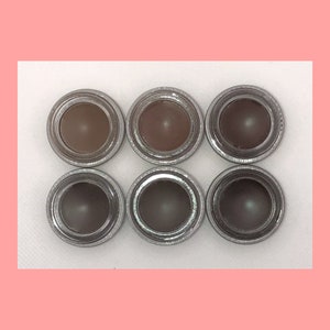 May include: Six small round pots of brown eyebrow gel, each in a silver container with a lid.