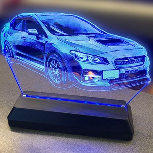 May include: A blue Subaru WRX STI car is etched into a clear acrylic base with a blue LED light strip. The base is black.