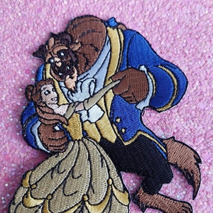 Può includere: Toppa ricamata raffigurante la Bestia e Belle de La Bella e la Bestia. La toppa raffigura i personaggi in una posa di danza, con la Bestia in un cappotto blu e Belle in un abito dorato. La toppa è realizzata con vari colori di filo.