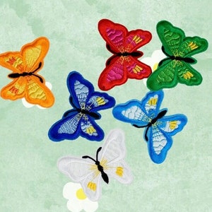 Può includere: Toppe ricamate a forma di farfalla in vari colori, tra cui arancione, rosso, verde, blu e bianco. Ogni farfalla presenta dettagliati motivi sulle ali e un corpo nero. Le toppe sono disposte su uno sfondo verde chiaro.