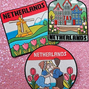 May include: Three embroidered patches, each with "NETHERLANDS" in bold text. One shows a windmill, another Dutch houses, and the third a kissing couple. All have red and white borders and are decorated with tulips.