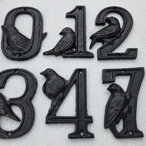May include: Black cast iron house numbers 0, 1, 2, 3, 4, and 7. Each number features a detailed bird perched on the number's frame. The numbers are designed for outdoor use and have a rustic, vintage aesthetic.