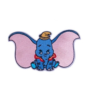 以下が含まれることがあります： 象のダンボの刺繍パッチ。パッチは、大きなピンクの耳、青い体、黄色の帽子をしたダンボが座っている様子を示しています。パッチは青いアウトラインと赤い襟を持っています。