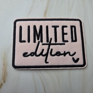 Può includere: Una toppa rettangolare con le parole "LIMITED edition" ricamate in nero su sfondo rosa chiaro. La toppa ha un bordo nero ed è probabilmente progettata per essere cucita su vestiti o accessori.