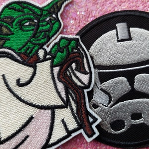 Puede incluir: Parches bordados con personajes de Star Wars. Un parche representa a Yoda en verde, blanco y marrón. Otro muestra un casco de Stormtrooper en gris y blanco sobre un fondo negro. Estos parches son ideales para personalizar ropa o accesorios.