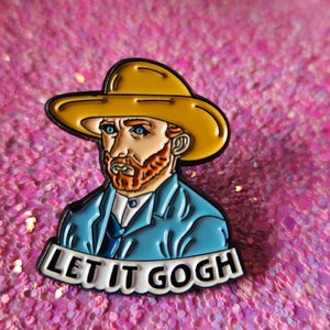 Op de afbeelding: Emaille pin met een cartoon van Vincent van Gogh met een gele hoed en blauwe jas. De tekst "LET IT GOGH" staat eronder. De pin is geplaatst tegen een roze glitterachtergrond.