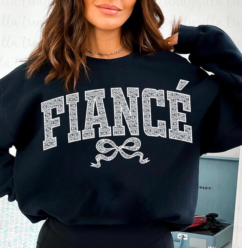 May include: Black sweatshirt with the word "FIANC&Eacute;" in white sparkly letters and a white sparkly bow underneath.