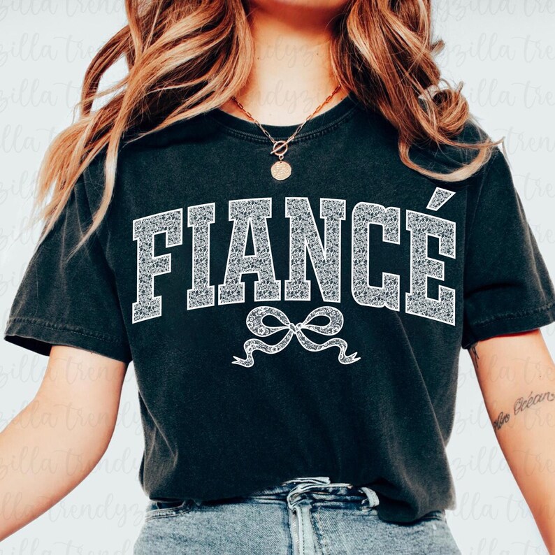 May include: Black t-shirt with white text that says "FIANC&Eacute;" in a large, bold font. A white bow is below the text.
