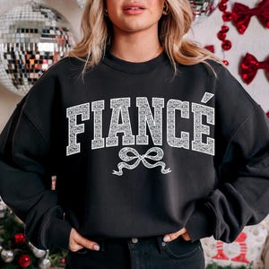 May include: Black sweatshirt with the word "FIANC&Eacute;" in white glitter letters with a white glitter bow underneath.