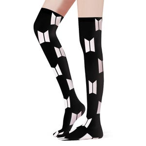 Peut inclure: Chaussettes hautes noires avec un motif géométrique blanc et rose clair répété. Les chaussettes s'étendent des pieds jusqu'à la mi-cuisse. Le motif est une série de formes de livres ouverts stylisés.