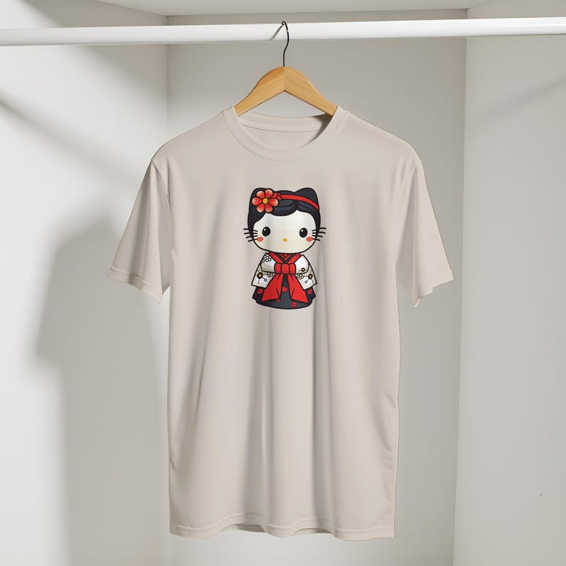 May include: A light beige t-shirt featuring a cartoon character in a traditional Japanese kimono. The character has a black bow, a red flower, and a red bow. The kimono is black and white with red accents. The shirt is hanging on a wooden hanger.