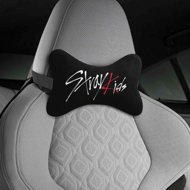 May include: Black car headrest pillow with the text "Stray Kids" in white and red script. The pillow is shaped like a bow tie and is placed on a light gray car seat with a diamond pattern.