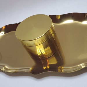 May include: A gold metal grinder and a gold metal tray. The grinder has a textured top and is sitting on the tray.