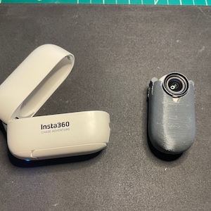 May include: A white Insta360 camera case with the text "Insta360 Chase Adventure" on the side, next to a grey camera with a black lens.