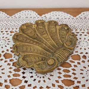 May include: A decorative brass dish with a scalloped edge and intricate floral design. The dish is made of a shiny, gold-coloured metal and has a vintage look.